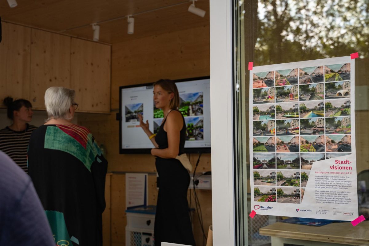 Eine Frau steht vor einem Bildschirm und präsentiert etwas. Man erkennt, dass es um Stadtvisionen und visualisierten Utopien geht. Man kann ZuhörerInnen erkennen.